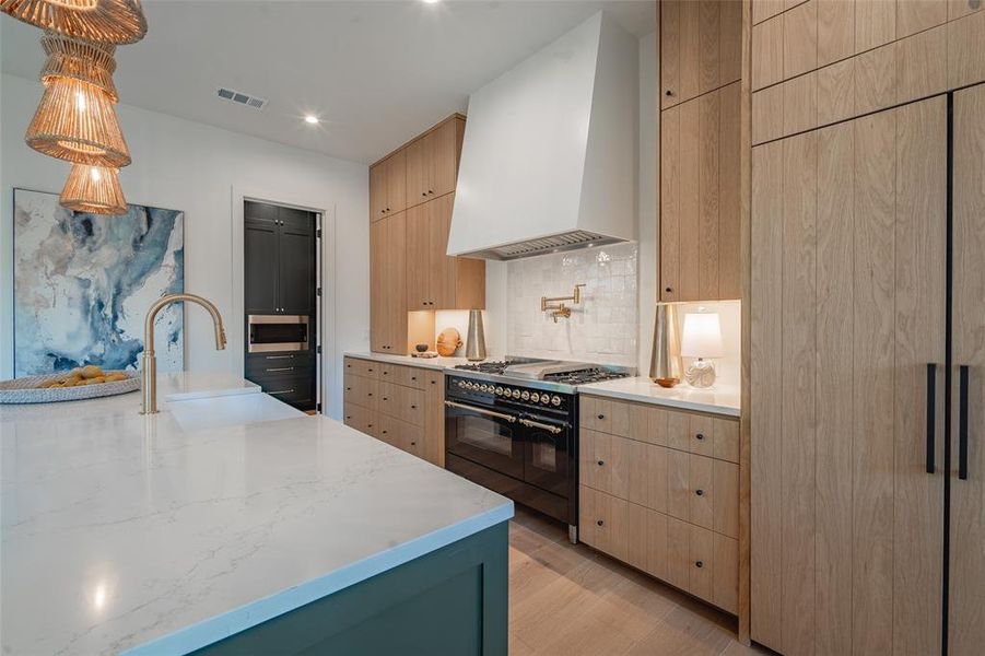 Kitchen with sink, range with two ovens, light brown cabinets, light hardwood / wood-style floors, and premium range hood