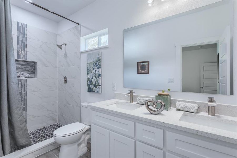 Bathroom featuring tiled shower, vanity, and toilet