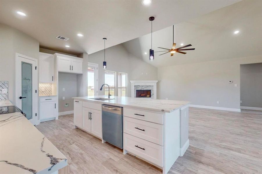 Kitchen with stainless steel dishwasher, a kitchen island with sink, a fireplace, and ceiling fan