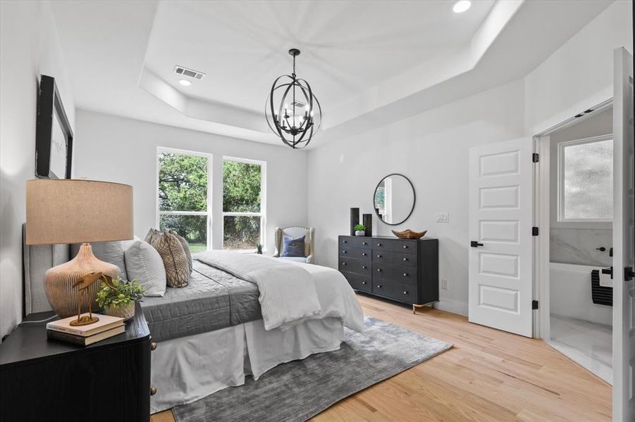 Bedroom with light wood-type flooring, a chandelier, and a tray ceiling