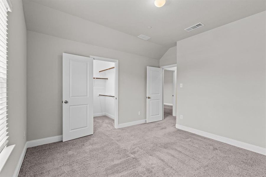 Unfurnished bedroom featuring lofted ceiling, a walk in closet, light colored carpet, and a closet