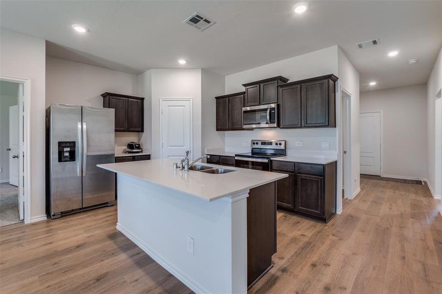 Kitchen featuring an island with sink, light hardwood / wood-style flooring, stainless steel appliances, sink, and dark brown cabinetry