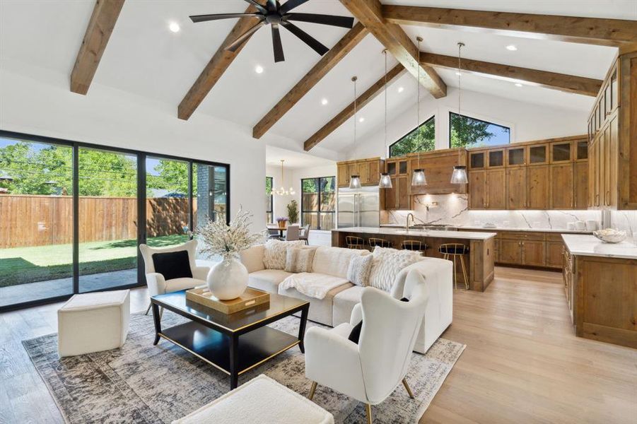 Living room with high vaulted ceiling, ceiling fan with notable chandelier, light hardwood / wood-style floors, and a healthy amount of sunlight