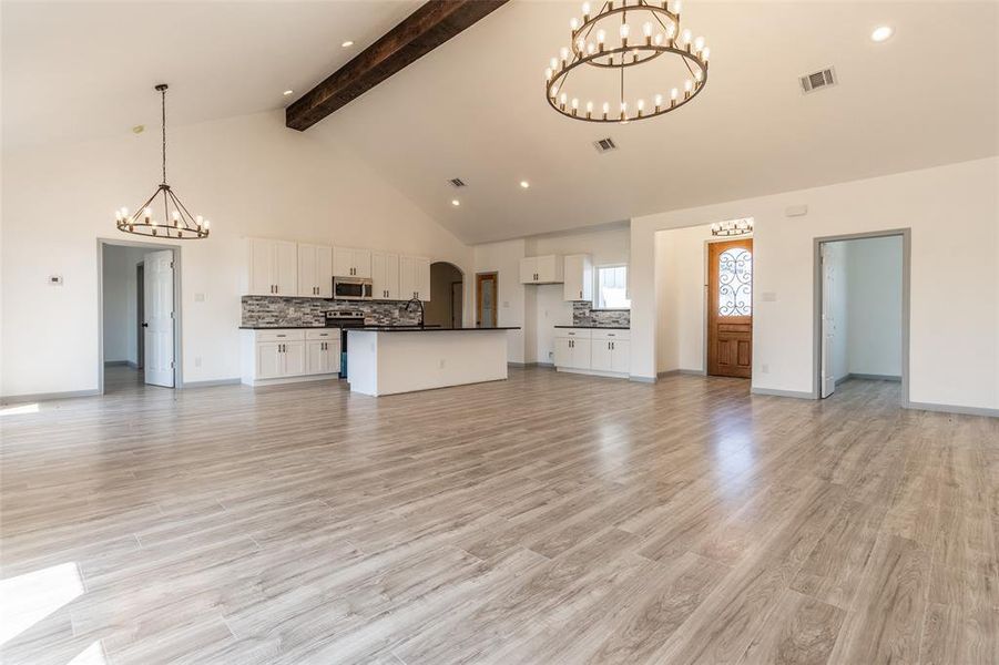 Unfurnished living room featuring beamed ceiling, high vaulted ceiling, a notable chandelier, light hardwood / wood-style flooring, and sink