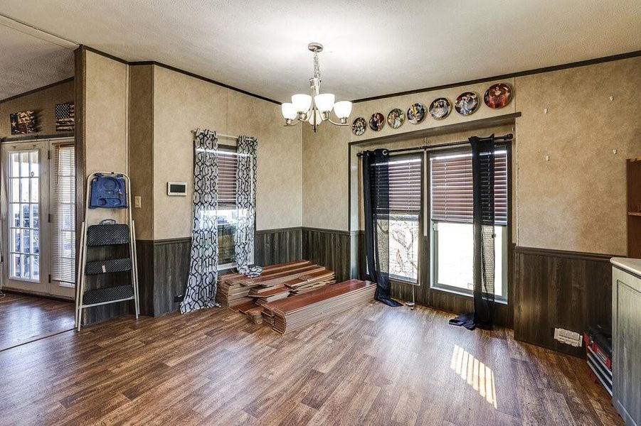 Unfurnished dining area featuring an inviting chandelier, wood-type flooring, a textured ceiling, and a healthy amount of sunlight