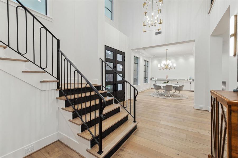 You are welcomed in thru custom black iron double doors with windows for natural light, leading to breathtaking wide plank French oak wood floors that set a luxurious tone. A large modern acrylic and brass pendant light illuminates the space, complementing the wood tread stairway adorned with black iron banister and contemporary sconce lighting for a warm, yet sophisticated ambiance.