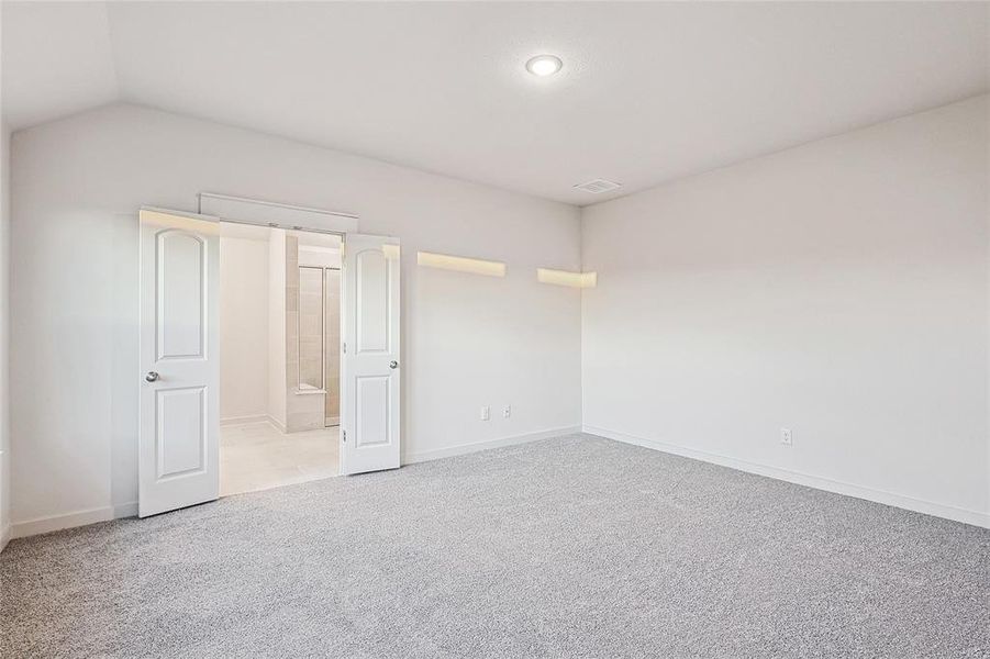 Unfurnished bedroom with connected bathroom, lofted ceiling, and light colored carpet