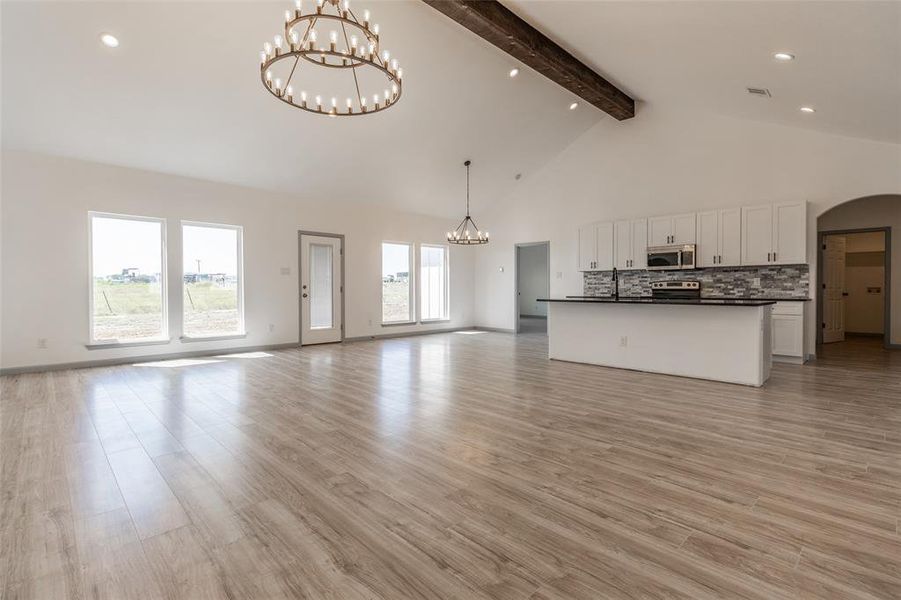 Unfurnished living room with beamed ceiling, a healthy amount of sunlight, high vaulted ceiling, and light hardwood / wood-style floors