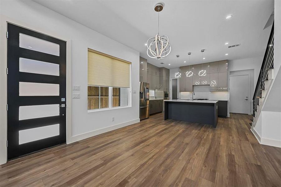 Kitchen with dark hardwood / wood-style floors, hanging light fixtures, a center island with sink, gray cabinets, and stainless steel refrigerator with ice dispenser