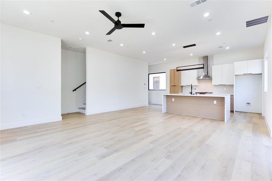 Kitchen featuring wall chimney range hood, light hardwood / wood-style floors, pendant lighting, a center island with sink, and white cabinetry