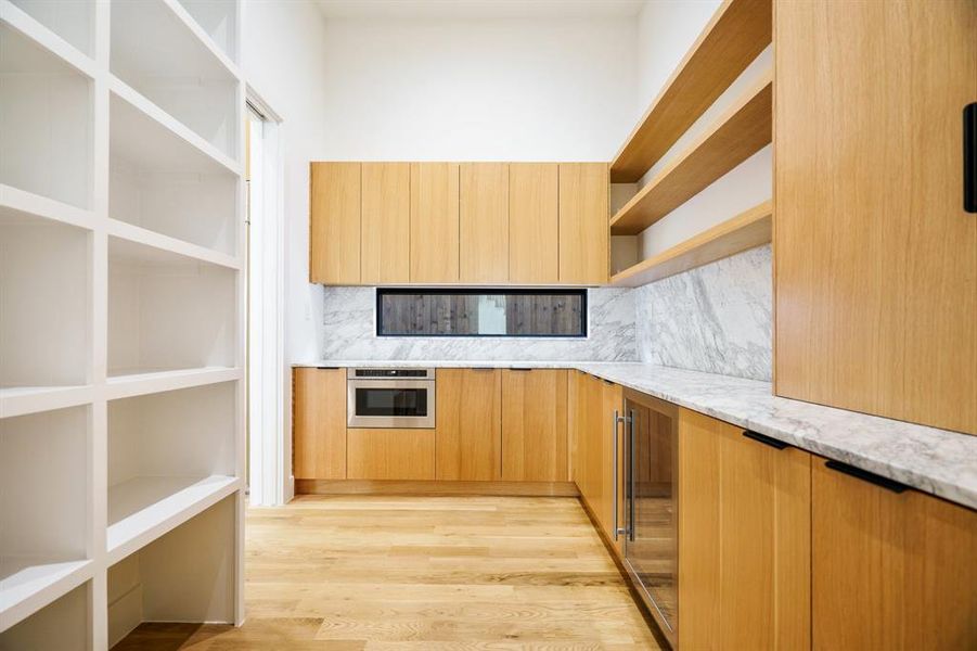 Kitchen with light wood-type flooring, light stone countertops, oven, wine cooler, and backsplash