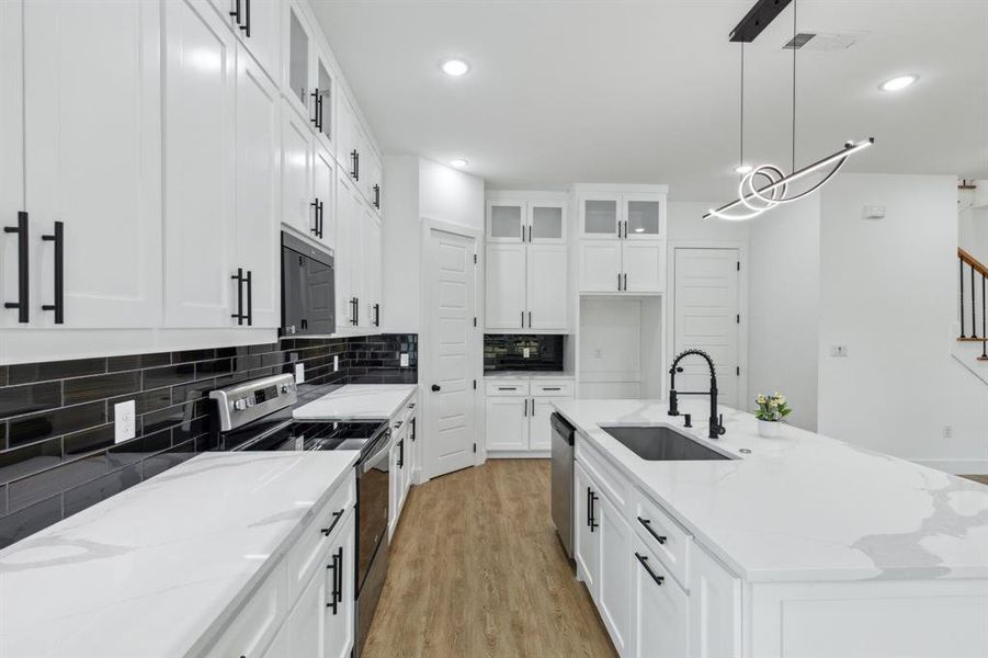 Kitchen with light stone counters, stainless steel appliances, light hardwood / wood-style floors, and an island with sink