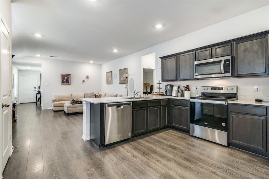 Kitchen featuring dark brown cabinets, dark hardwood / wood-style floors, sink, kitchen peninsula, and appliances with stainless steel finishes