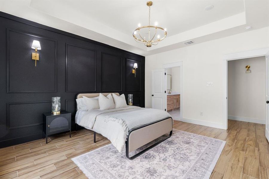 Bedroom with an inviting chandelier, connected bathroom, light hardwood / wood-style flooring, and a raised ceiling