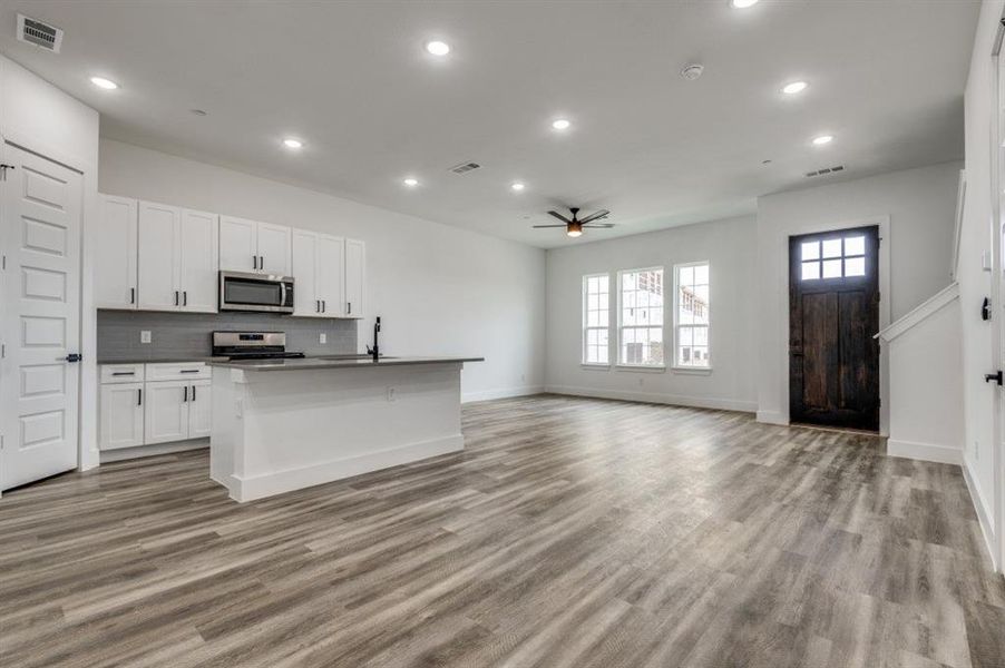 Kitchen with white cabinets, an island with sink, ceiling fan, light wood-type flooring, and appliances with stainless steel finishes