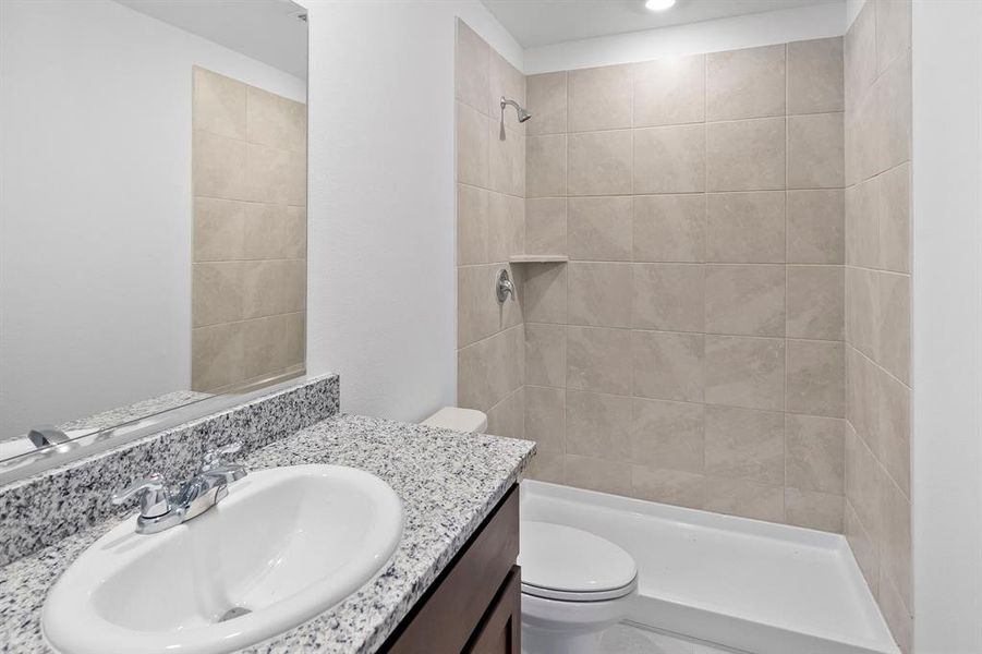 Bathroom featuring a tile shower, vanity, and toilet