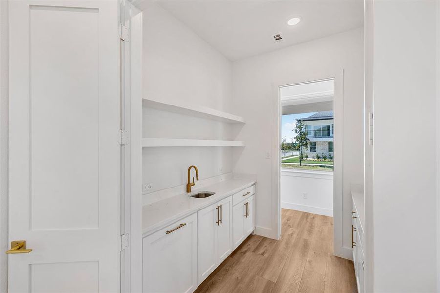 Bar with white cabinetry, light hardwood / wood-style flooring, and sink