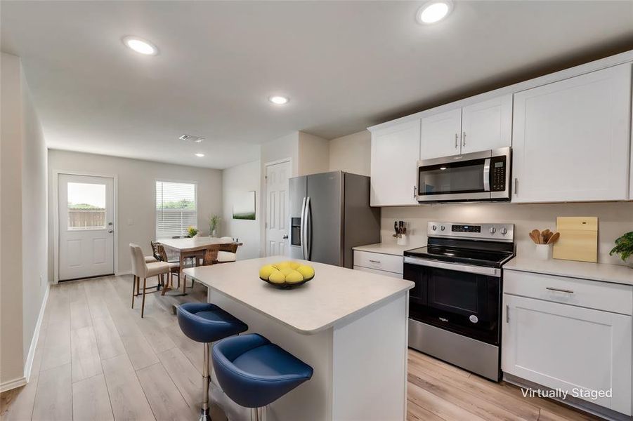 Kitchen with a kitchen island, LVP flooring, stainless steel appliances, white cabinets, and a kitchen bar