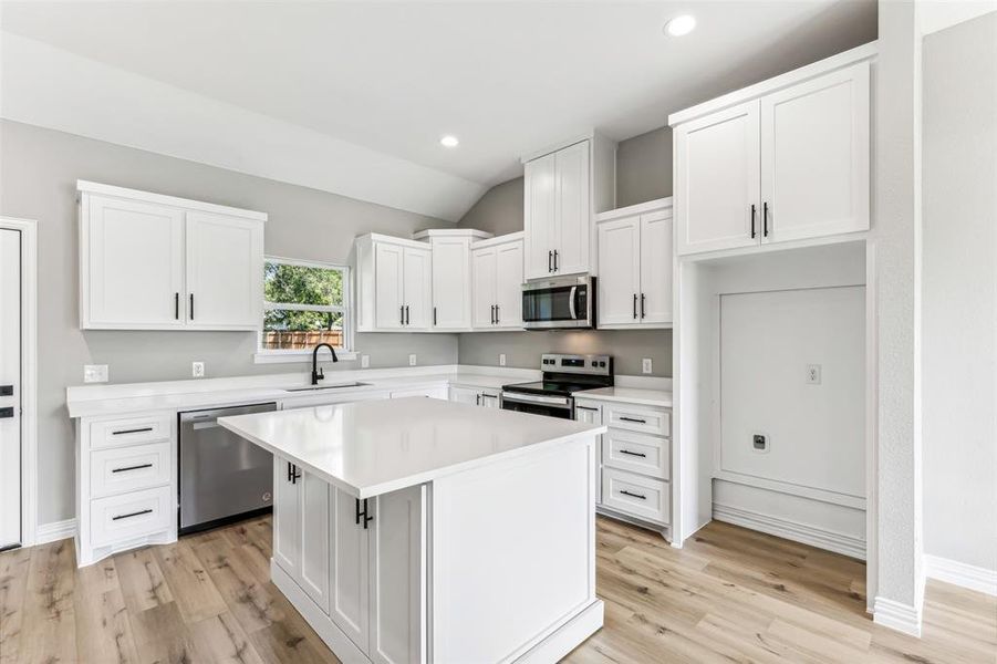 Kitchen featuring a kitchen island, appliances with stainless steel finishes, sink, white cabinetry, and lofted ceiling