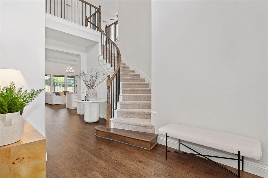 Stairway with an inviting chandelier, wood-type flooring, and a towering ceiling