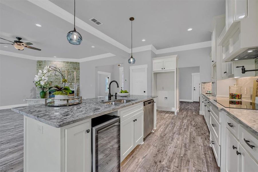 Kitchen with wine cooler, white cabinetry, a kitchen island with sink, and sink