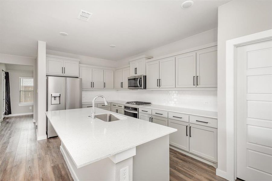 Kitchen featuring stainless steel appliances, hardwood / wood-style floors, sink, backsplash, and a kitchen island with sink