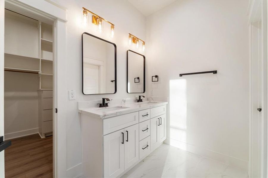 The primary bathroom features dual sinks, ample storage, and modern mirrors. Two vanity lights illuminate the area, which also includes a walk-in shower and private water closet.