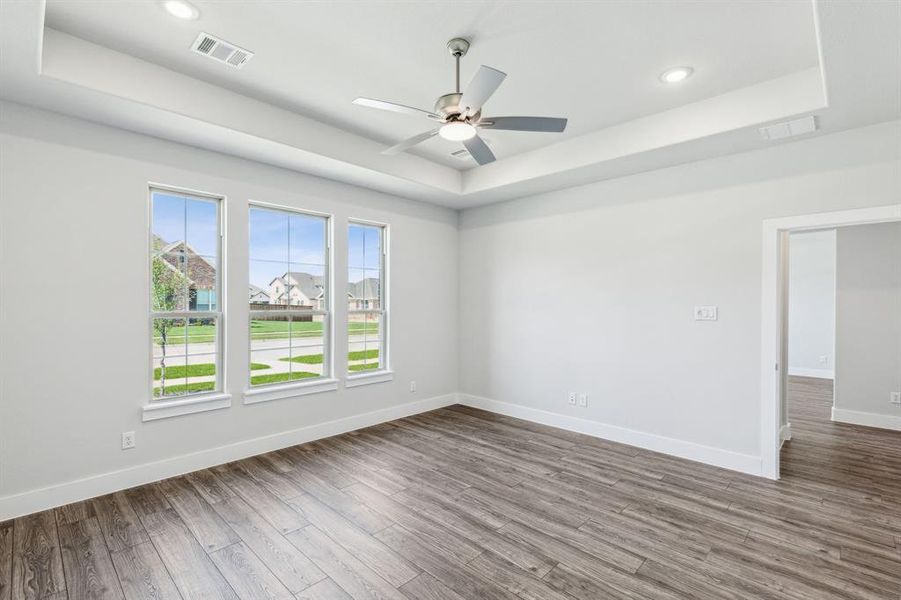 Empty room with a raised ceiling, ceiling fan, and wood-type flooring