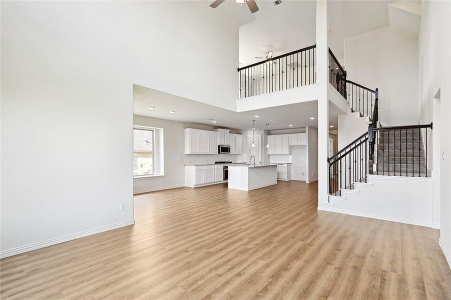 Unfurnished living room featuring light wood-type flooring, a high ceiling, sink, and ceiling fan