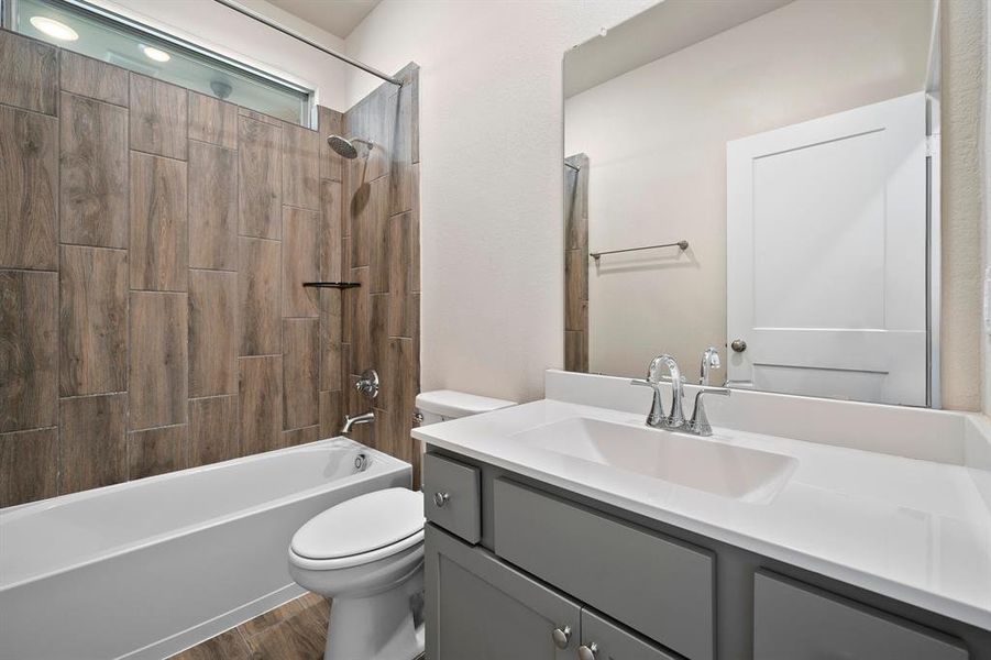 Secondary bathroom features light countertops and grey cabinets, neutral paint, shower/tub combo with tile surround, large mirror, tile floors, sleek fixtures and plenty of space to accommodate any visiting family or guests.