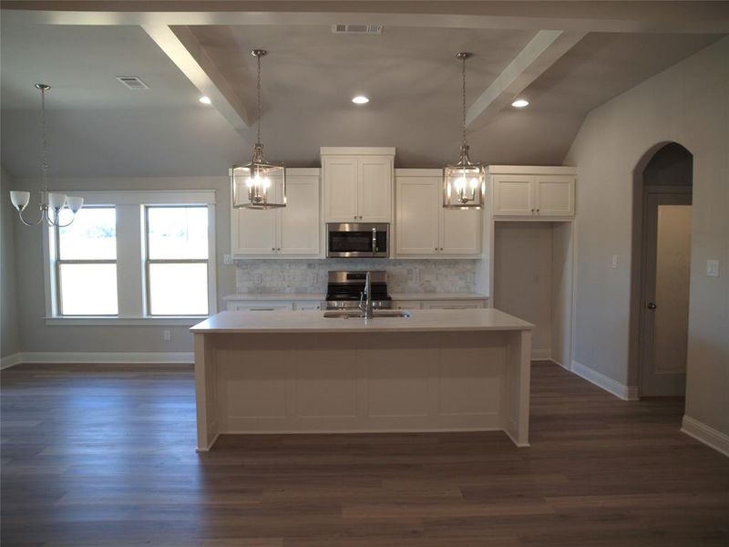 Kitchen with appliances with stainless steel finishes, a kitchen island with sink, lofted ceiling with beams, and white cabinetry