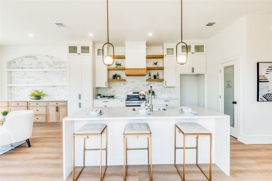 Kitchen featuring an island with sink, hanging light fixtures, sink, and light hardwood / wood-style flooring