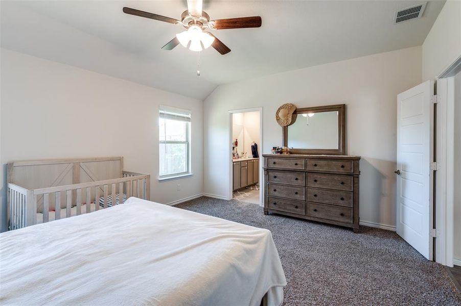 Bedroom featuring dark colored carpet, connected bathroom, vaulted ceiling, and ceiling fan