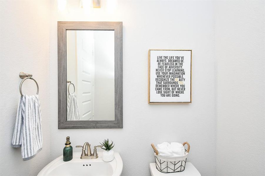 Half bath off of the living area. It features a pedestal sink and framed mirror.