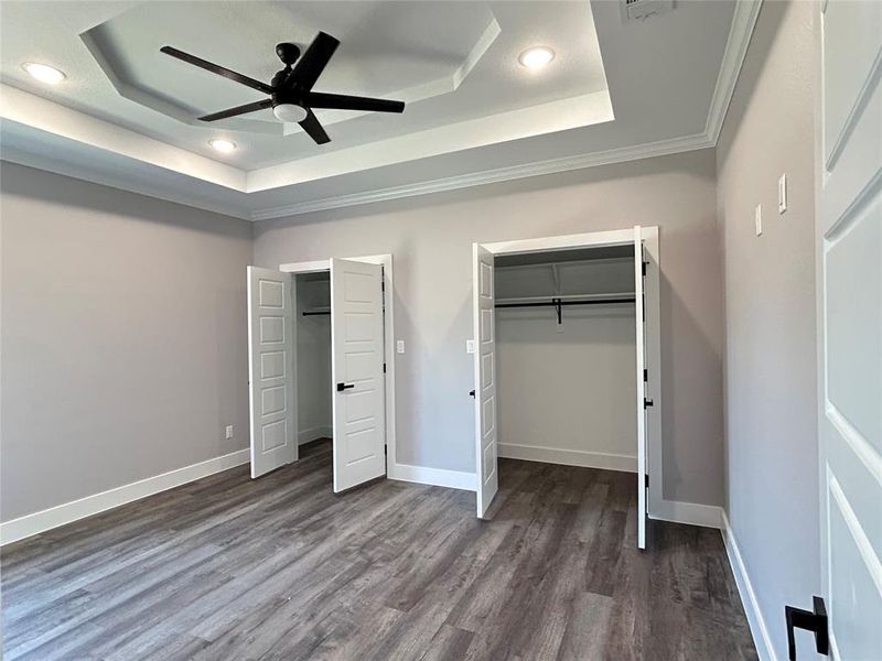 Unfurnished bedroom featuring ceiling fan, a raised ceiling, ornamental molding, and dark hardwood / wood-style flooring