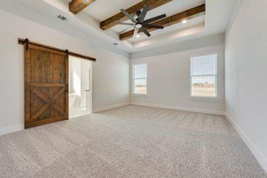 Empty room featuring beam ceiling, a barn door, a healthy amount of sunlight, and ceiling fan