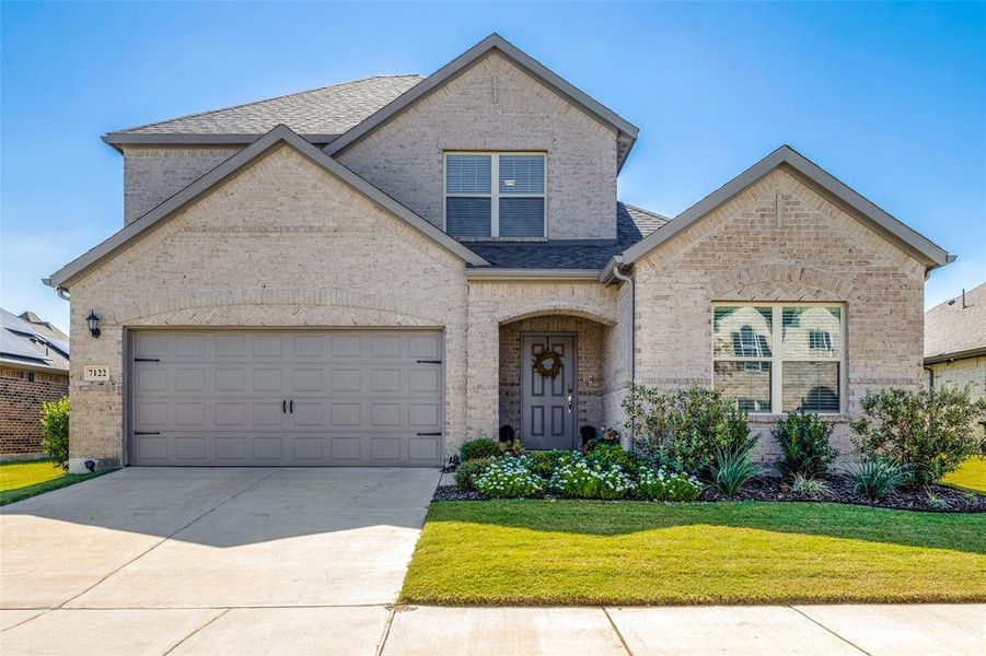 View of front of home featuring a two car garage and lush front lawn with sprinkler system