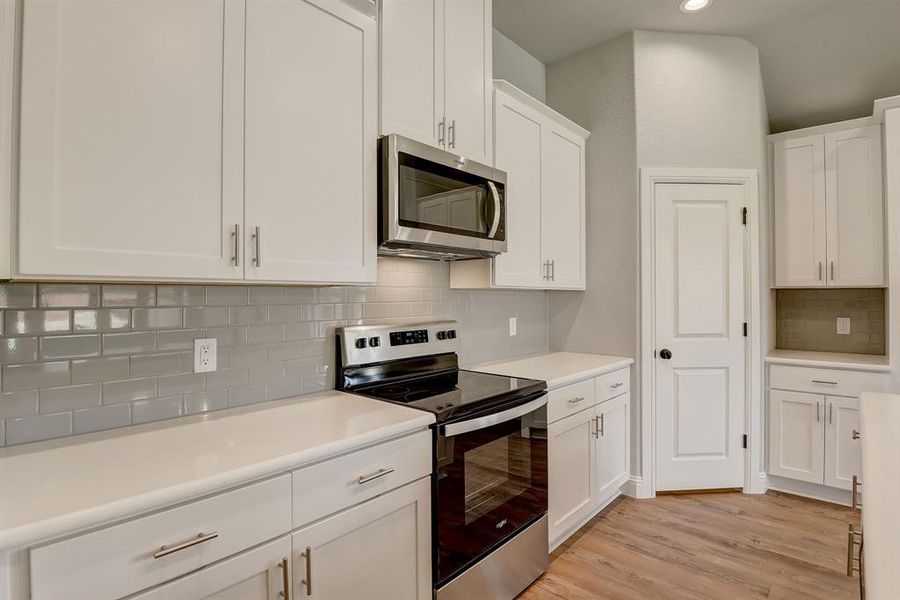 Kitchen featuring white cabinets, appliances with stainless steel finishes, light hardwood / wood-style flooring, and tasteful backsplash