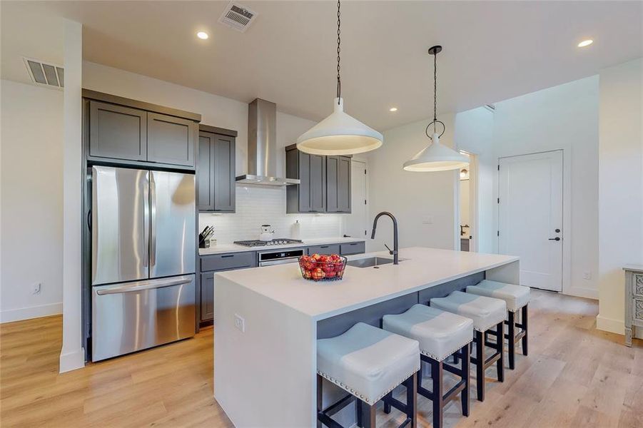 Kitchen featuring tasteful backsplash, stainless steel refrigerator, light wood-type flooring, wall chimney exhaust hood, and sink