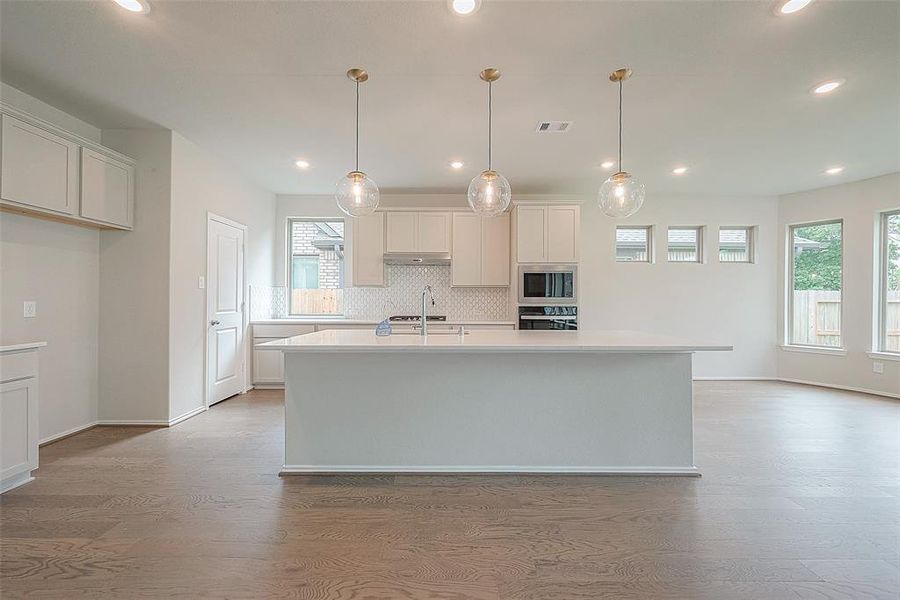 Culinary delights await in the gourmet kitchen, equipped with a oversized island, elegant pendant lighting, granite countertops, designer tile backsplash, and built-in stainless-steel appliances including a gas hooded range.