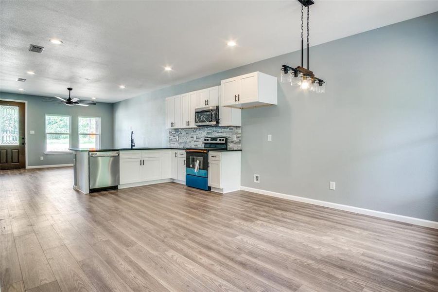 Kitchen with white cabinetry, stainless steel appliances, light hardwood / wood-style floors, and pendant lighting