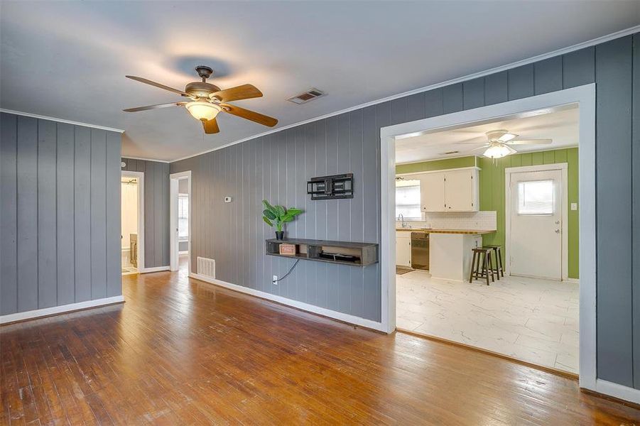 Unfurnished living room featuring wood walls, ornamental molding, hardwood / wood-style flooring, and ceiling fan