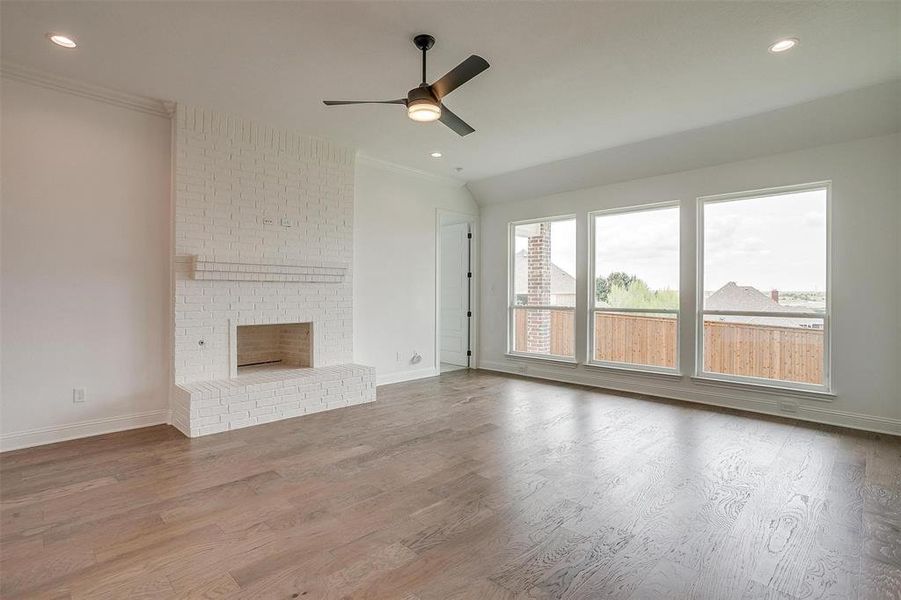 Unfurnished living room featuring a fireplace, crown molding, hardwood / wood-style flooring, and ceiling fan