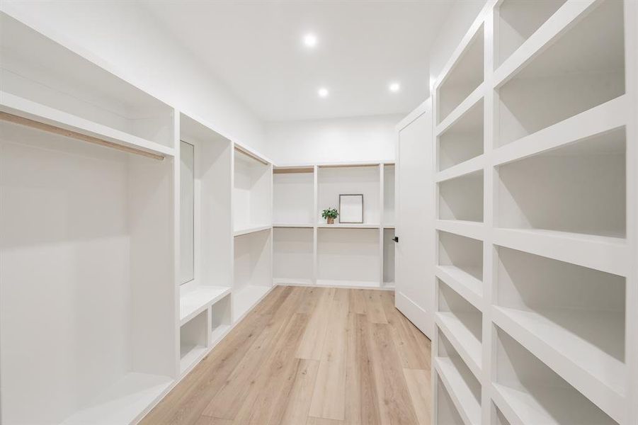 Spacious closet featuring spectacular built-ins, blonde plank, wood-like luxury vinyl floors. Truly a home owners dream closet with season storage racks above.