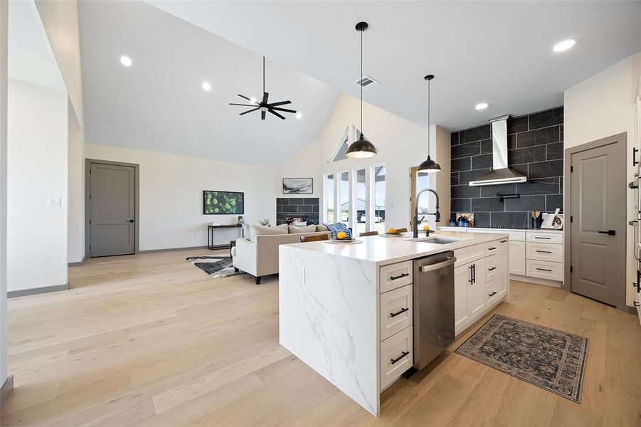 Kitchen with wall chimney range hood, a center island with sink, ceiling fan, light hardwood / wood-style flooring, and a tile fireplace