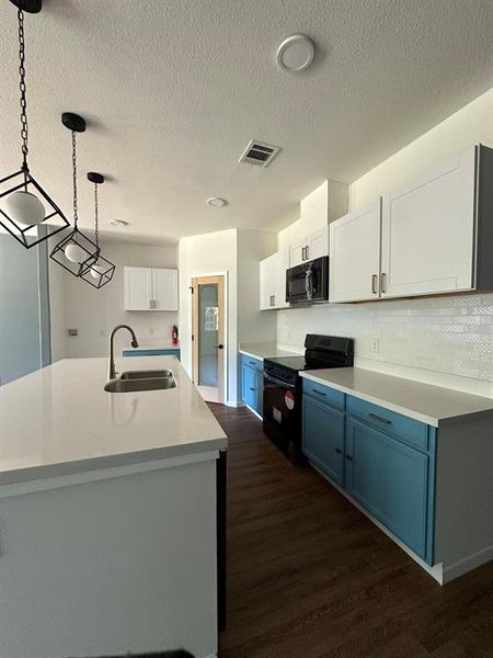 Kitchen featuring dark hardwood / wood-style floors, hanging light fixtures, white cabinetry, black appliances, and sink