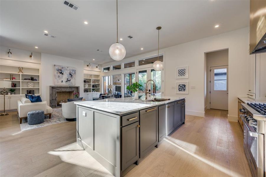 Kitchen featuring an island with sink, sink, a high end fireplace, light stone countertops, and light hardwood / wood-style floors