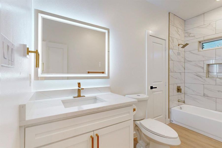 Full bathroom featuring vanity, wood-type flooring, tiled shower / bath combo, and toilet