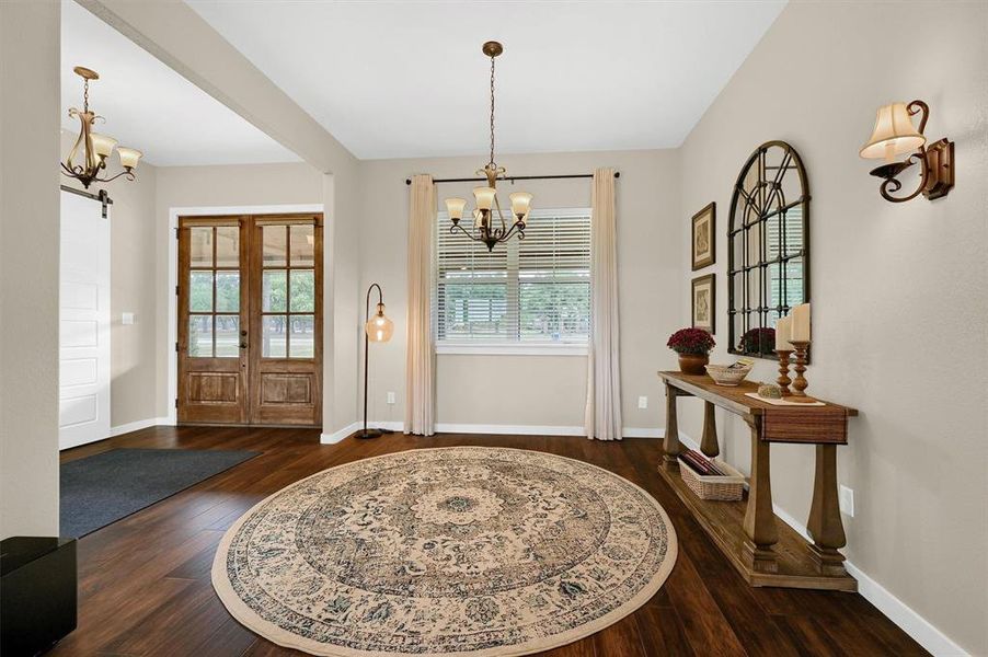 Foyer entrance with an inviting chandelier, dark wood-type flooring, a barn door, and french doors