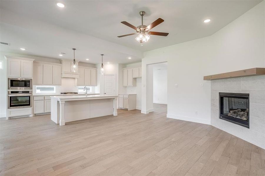 Kitchen featuring light hardwood / wood-style floors, a fireplace, stainless steel appliances, a center island with sink, and ceiling fan